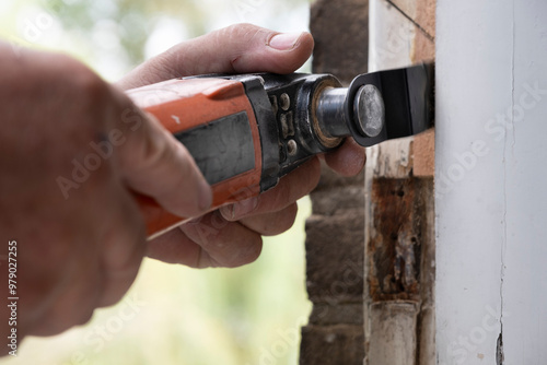 Carpenter cuts a piece of rotten wood from a window frame with an oscillating renovator saw, the unique system for remodeling and renovation