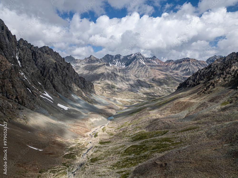 Aerial view of snowy mountains and a serene valley under dramatic clouds, Deosai National Park, Skardu, Pakistan. Aerial view of snowy mountains and a serene valley under dramatic clouds, Deosai National Park, Skardu, Pakistan.