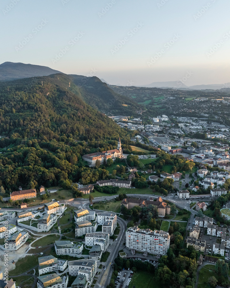 Aerial view of the beautiful historic cityscape featuring the Basilique de la Visitation surrounded by mountains and greenery at sunset, Annecy, France. Aerial view of the beautiful historic cityscape featuring the Basilique de la Visitation surrounded by mountains and greenery at sunset, Annecy, France.