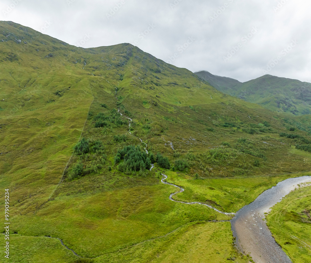 Aerial view of a majestic waterfall cascading into a winding river surrounded by lush green mountains, Kyle, Scotland, United Kingdom. Aerial view of a majestic waterfall cascading into a winding river surrounded by lush green mountains, Kyle, Scotland, United Kingdom.