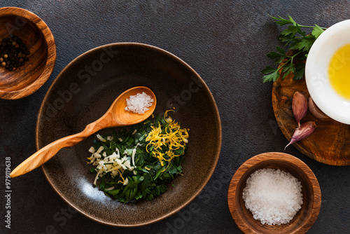 Fresh parsley, lemon, garlic in ceramic bowl over dark background, gremolata ingredients photo