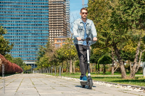 Man riding e-scooter in city public park at sunny summer day. Male driving electric scooter enjoying leisurely outdoor ride. Eco-friendly city transport and travel. Sustainable lifestyle concept