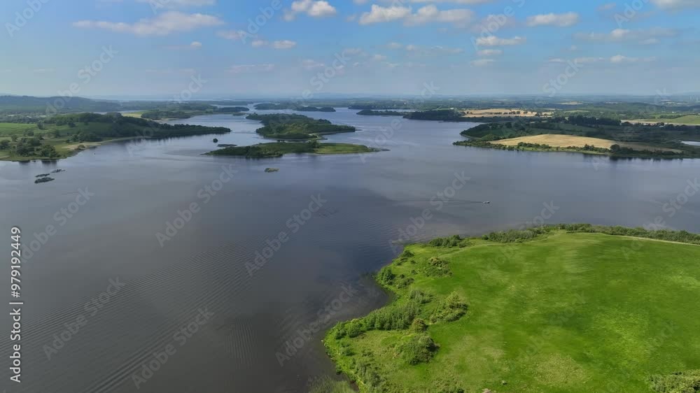 Lower Lough Erne, County Fermanagh, Northern Ireland, June 2023. Drone pushes forward establishing overview above islands on the lake sloping down to the glistening lakeshore. Lower Lough Erne, County Fermanagh, Northern Ireland, June 2023. Drone pushes forward establishing overview above islands on the lake sloping down to the glistening lakeshore.