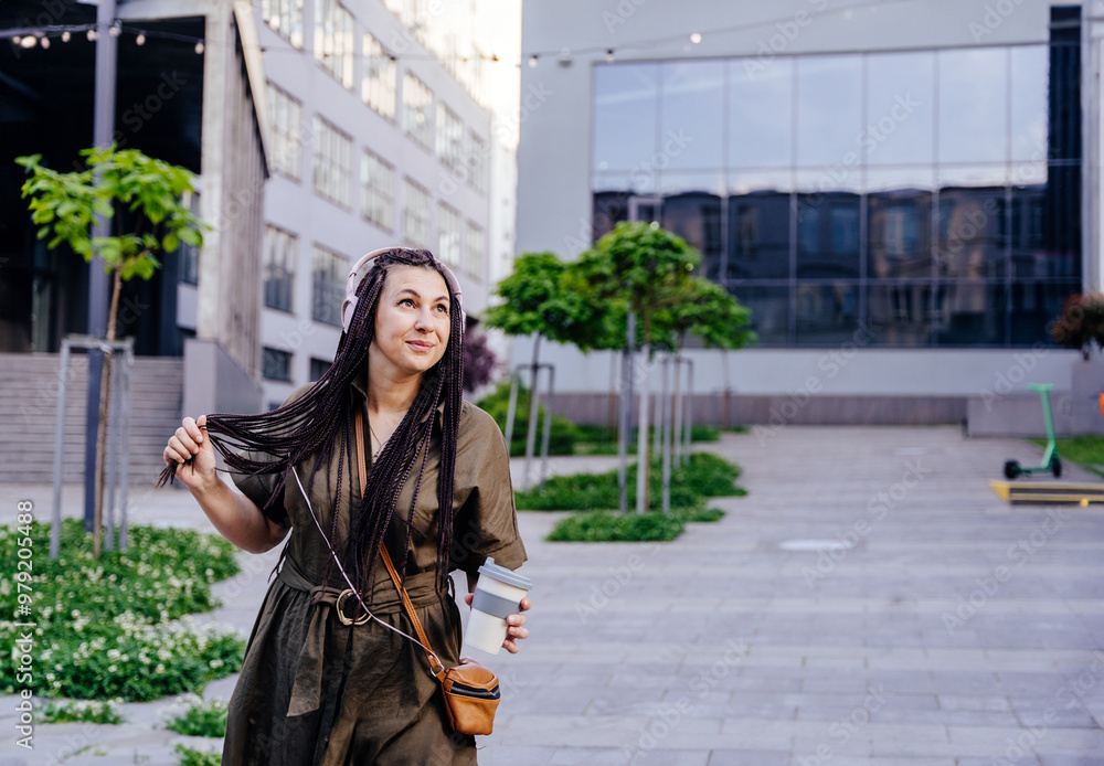 Fototapeta premium Happy mid adult woman enjoying listening to music through headphones outdoor.