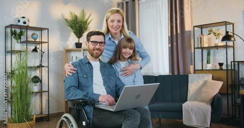 Family portrait of man in wheelchair his loving woman wife and teenage daughter looking at camera with sincerely smiles photo