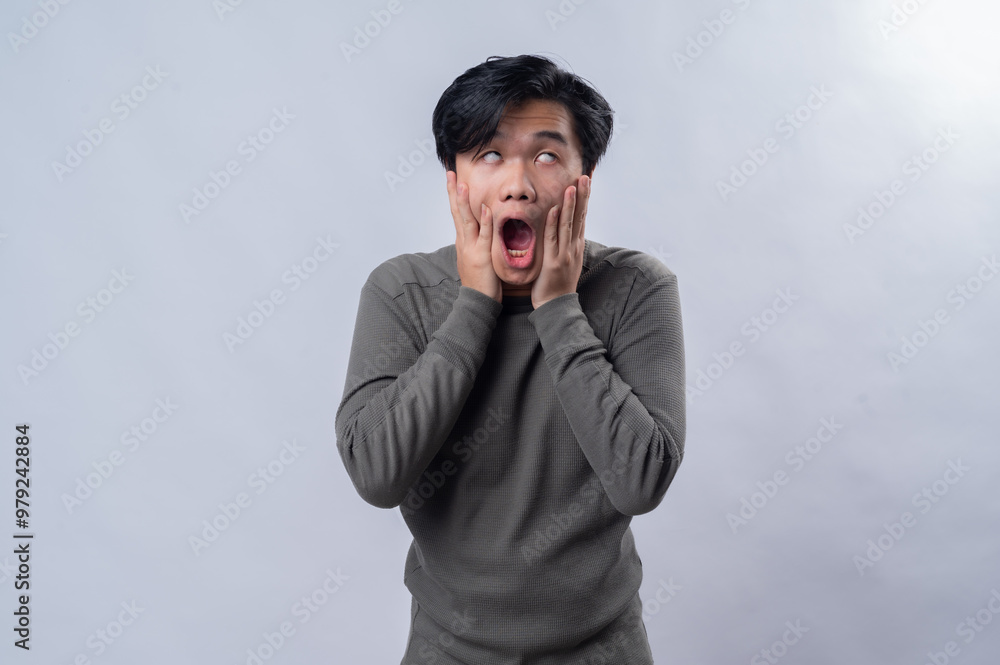 A surprised and shocked Asian man wearing a casual long-sleeve gray shirt, holding both hands to his face with wide eyes and open mouth. Captured in a studio setting with a plain white background A surprised and shocked Asian man wearing a casual long-sleeve gray shirt, holding both hands to his face with wide eyes and open mouth. Captured in a studio setting with a plain white background