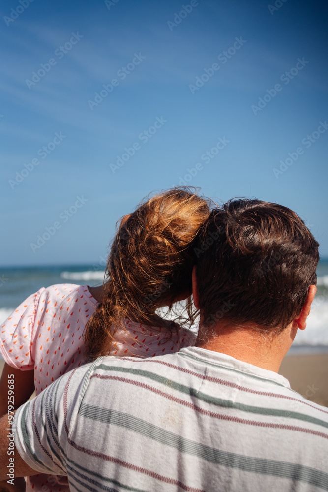 Fototapeta premium Father and daughter stand on the beach, gazing at the waves, sharing a moment of reflection by the ocean