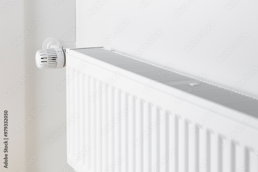 A close-up of a radiator with a temperature control dial mounted on a white wall A close-up of a radiator with a temperature control dial mounted on a white wall