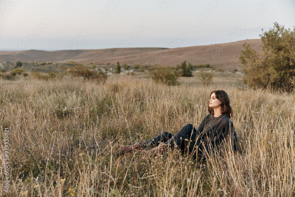 Serene woman enjoying nature as the sun sets over a grassy hill in the countryside Serene woman enjoying nature as the sun sets over a grassy hill in the countryside