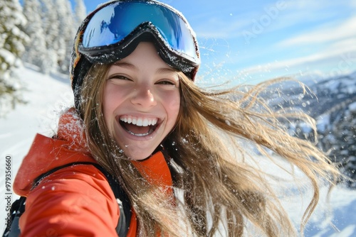 A young woman in ski goggles laughs with windswept hair.