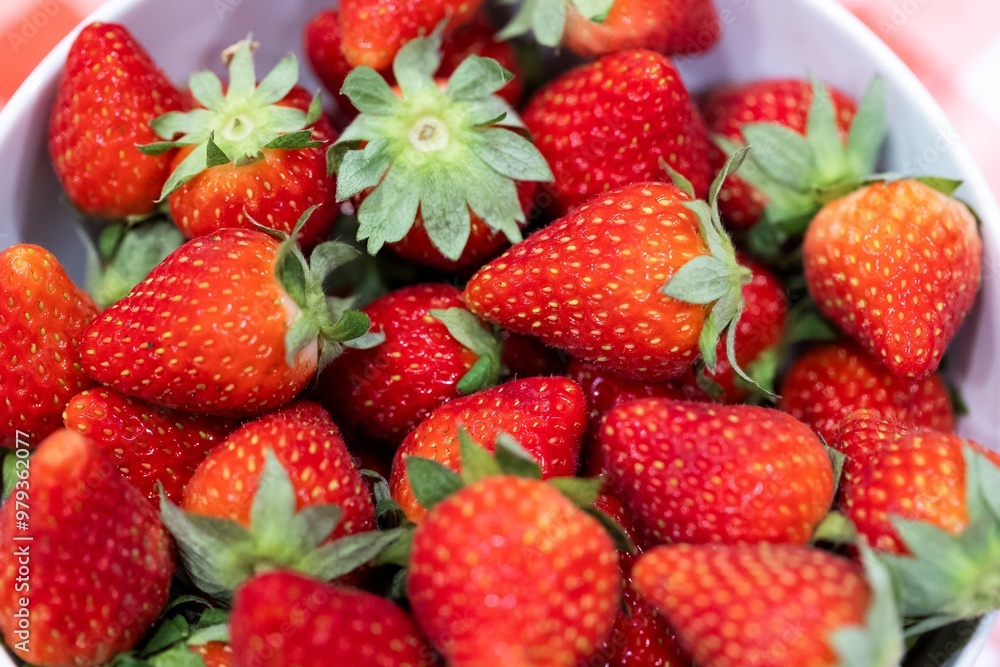 A portrait of a bunch of red delicious fresh strawberies with the green top in a white bowl. The tasty fruit is ready to be eaten. A portrait of a bunch of red delicious fresh strawberies with the green top in a white bowl. The tasty fruit is ready to be eaten.