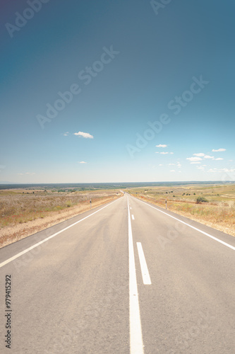 Stunning image of a long, open road stretching into the horizon under a clear blue sky, embodying the spirit of travel and adventure. The scenic countryside setting evokes a sense of freedom.