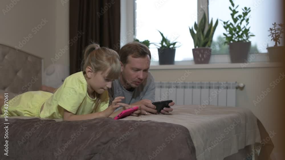 Dad and daughter sit at home and play video games on a mobile phone Dad and daughter sit at home and play video games on a mobile phone