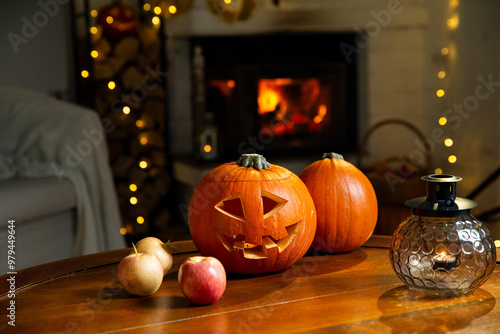 Halloween pumpkin jack-o'-lantern on old wooden table with burning fire place background in a living room on the eve of Halloween, holiday vibes