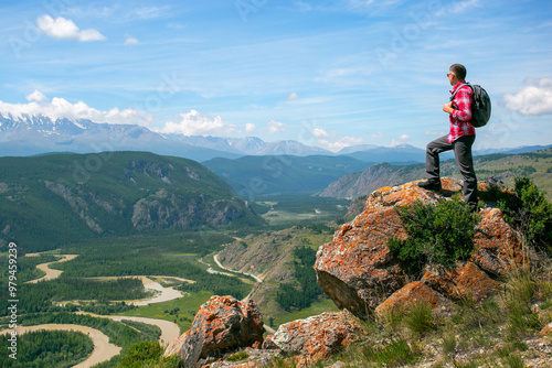 Hiker with backpack relaxing on top of a mountain and enjoying valley view.