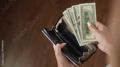 Woman counting 100 us dollar bills while holding a leather wallet. The scene captures the essence of managing cash and reflects themes of finance and wealth photo