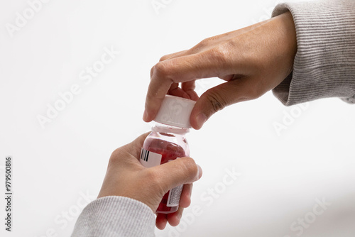 Someone is twisting open the cap of a cough syrup bottle containing bright red liquid.