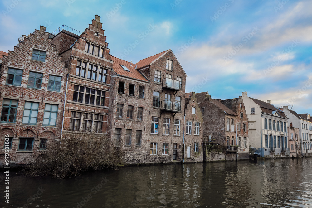Historic brick buildings along the canal in Ghent showcase the city's architectural charm during a calm afternoon Historic brick buildings along the canal in Ghent showcase the city's architectural charm during a calm afternoon