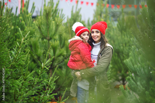 mother holds her daughter in her arms against the backdrop of many Christmas trees and snow.