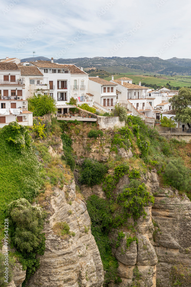 View of picturesque houses on a dramatic cliff surrounded by greenery under a sunny sky, Ronda, Spain. View of picturesque houses on a dramatic cliff surrounded by greenery under a sunny sky, Ronda, Spain.