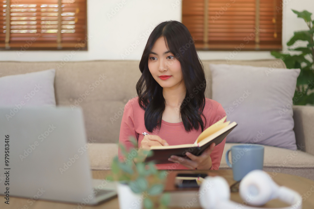 Young businesswoman working at home to reading business data on laptop and writing note in notebook Young businesswoman working at home to reading business data on laptop and writing note in notebook