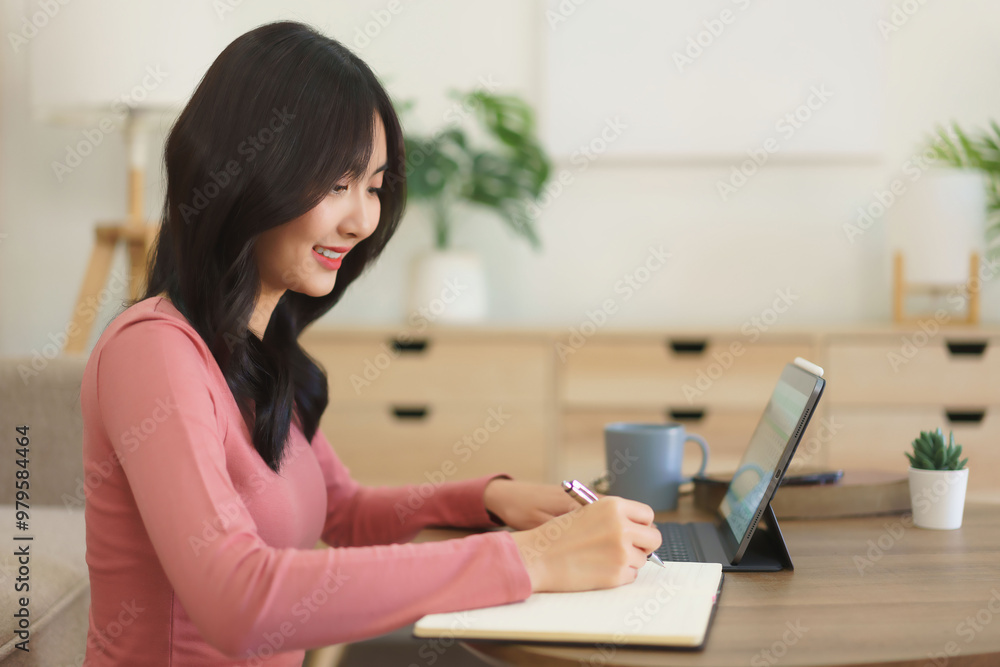 Young businesswoman searching data on tablet and writing down idea in paper while working at home Young businesswoman searching data on tablet and writing down idea in paper while working at home