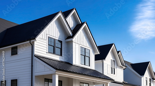 Modern two-story white houses with black roofing and windows, featuring contemporary architectural design under a clear blue sky.