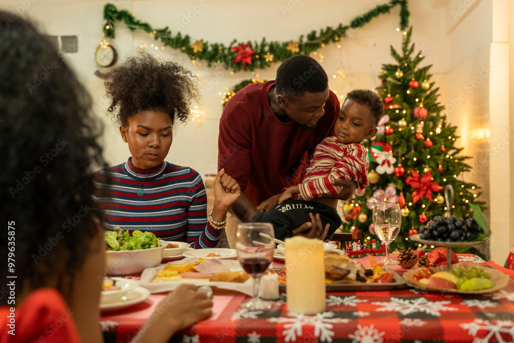 A joyful family gathers around the dinner table celebrating Christmas. The father, dressed in a Santa hat, gives a gift to the child, while everyone smiles with warmth and festive decorations. A joyful family gathers around the dinner table celebrating Christmas. The father, dressed in a Santa hat, gives a gift to the child, while everyone smiles with warmth and festive decorations.