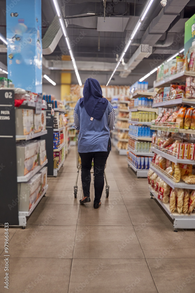 Asian woman wearing hijab shopping at supermarket looking for daily needs between store shelves Asian woman wearing hijab shopping at supermarket looking for daily needs between store shelves