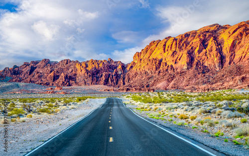 Winding road through Valley of Fire State Park, just north of Las Vegas in Southern Nevada with vibrant orange sandstone mountains and a partly cloudy sky in the background.