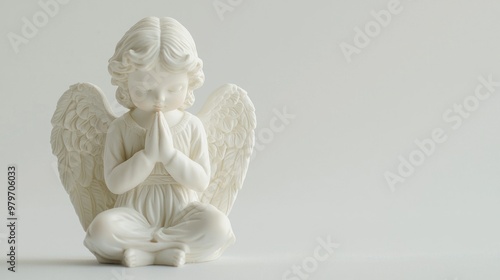 A close-up of a delicate angel figurine with hands folded in prayer, softly lit against a plain white background.