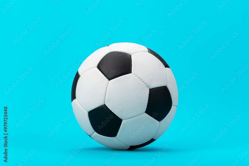 Fototapeta premium Photo of white and black soccer ball as football concept. Minimalist image of leather football ball over blue turquoise background with central composition.