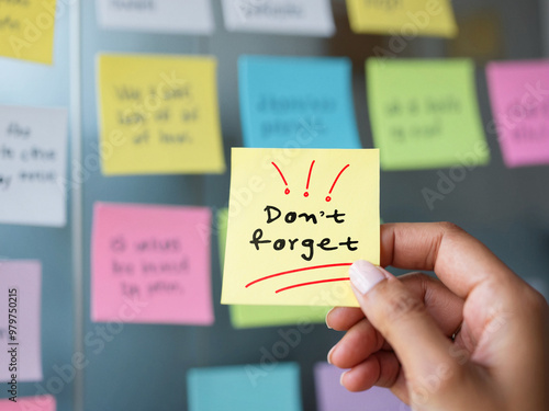 Close-up of a hand holding a sticky note with "Don't forget" written, important reminder in an office environment, colorful sticky notes in the background, focus on organization and memory
