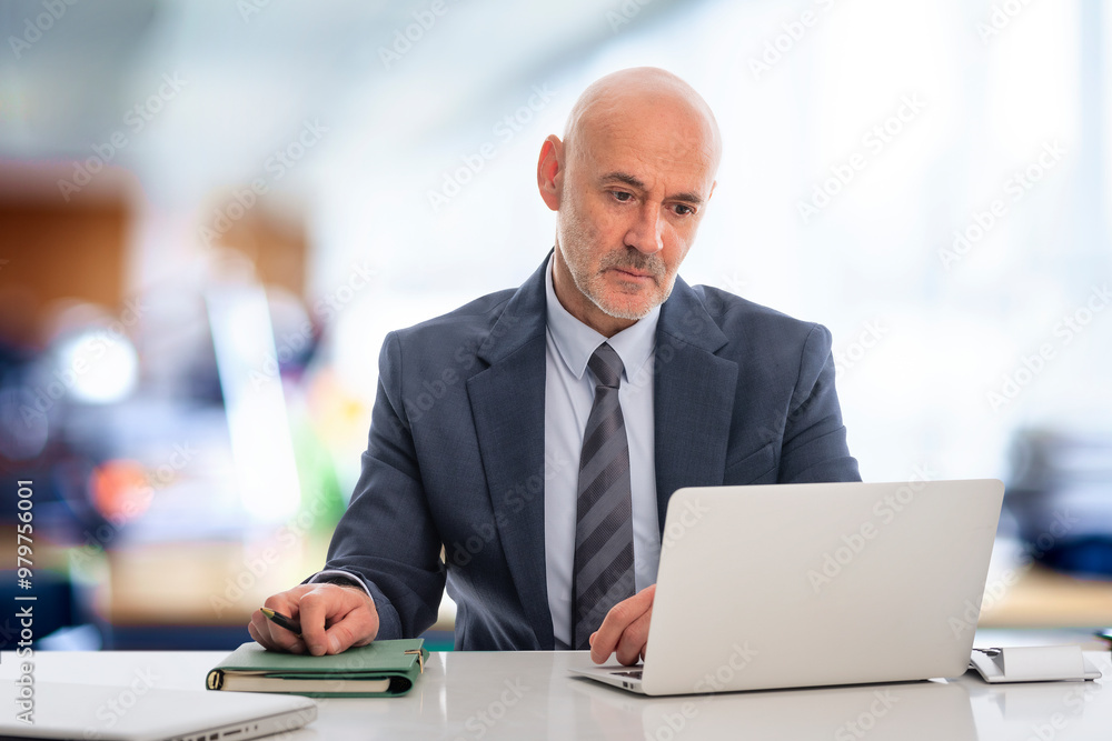Senior businessman sitting at the office and looking his notebook thoughtfully Senior businessman sitting at the office and looking his notebook thoughtfully