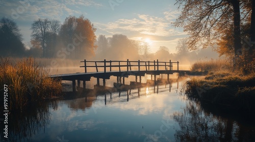Sunrise over a calm river and lake with reflections of trees and mist in the morning sky and bridge.