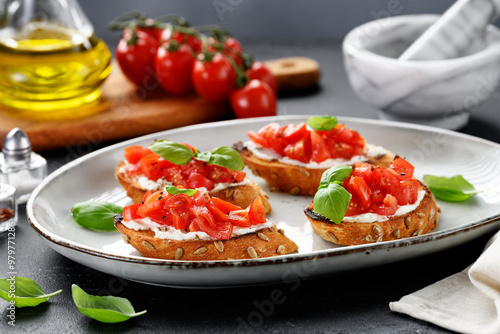 Cherry tomatoes and cream cheese bruschettas with fresh basil leaves.