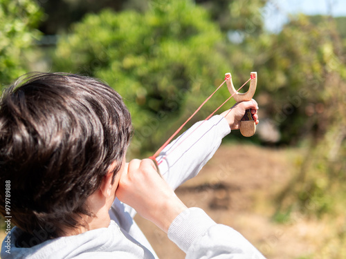 Tableau sur toile Boy aiming a slingshot in a sunny outdoor environment