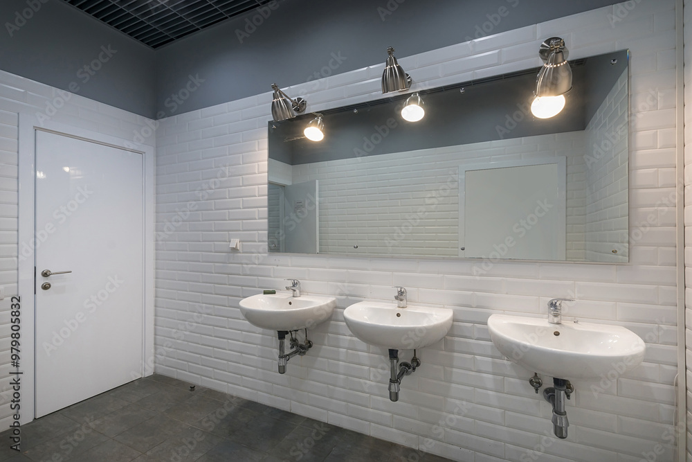 © alhim - Office public bathroom, decorated with white tiles. A large mirror and three sinks.