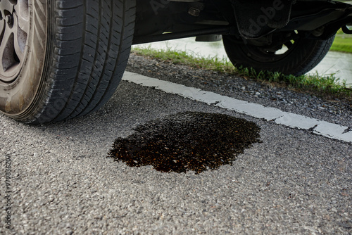 Black engine oil stains dripped under a broken down car parked on the road. Concept of car repair and maintenance