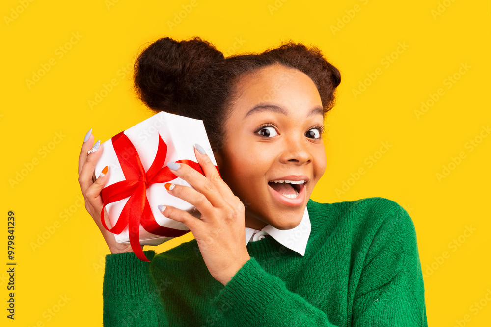 Xmas Present. Curious black teen girl shaking box, checking gift over yellow background, panorama, free space Xmas Present. Curious black teen girl shaking box, checking gift over yellow background, panorama, free space