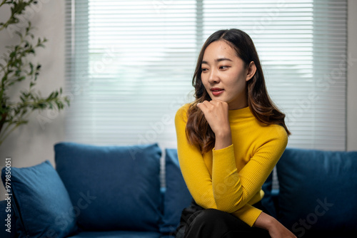 Young asian woman sitting on sofa is thinking at home