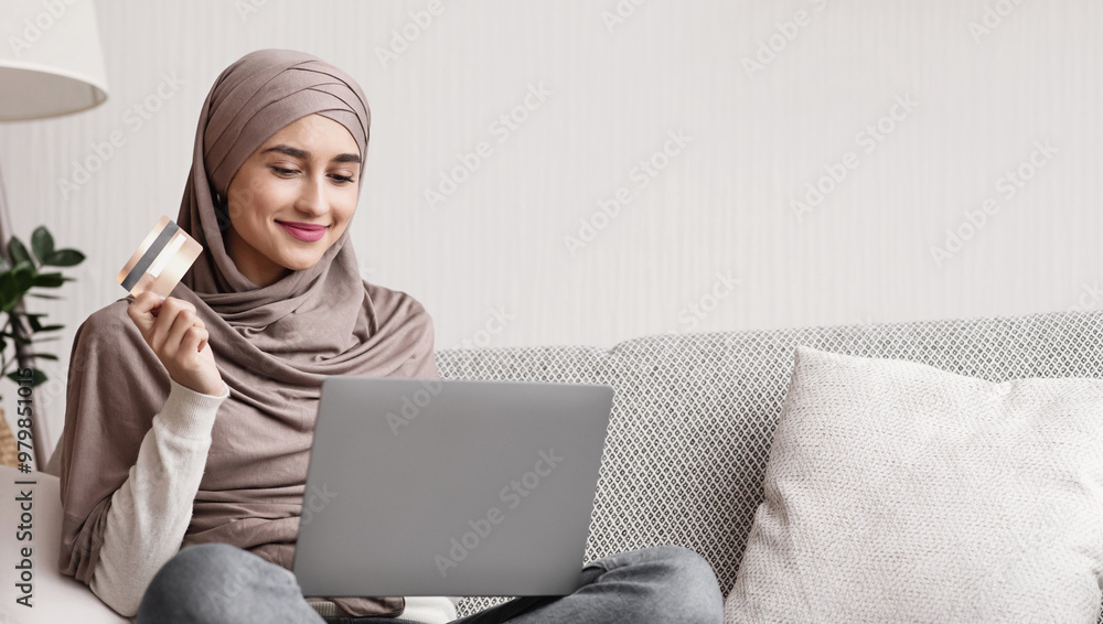 Easy payments. Smiling arabic woman in headscarf using laptop and credit card at home, paying for utilities online, free space Easy payments. Smiling arabic woman in headscarf using laptop and credit card at home, paying for utilities online, free space