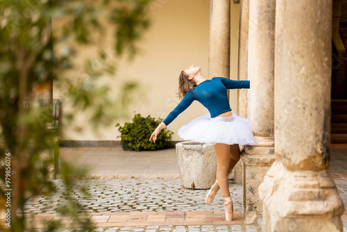 A young 20-year-old girl is doing poses in professional ballet clothes outdoors at an architectural site.The female dancer does a pose called cambre.Outdoor ballet concept. photo