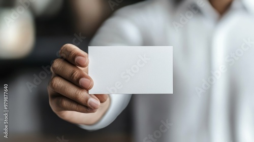 Confident businessman holds blank business card in office setting, ideal for customizing with your design. Professional scene conveys success and communication