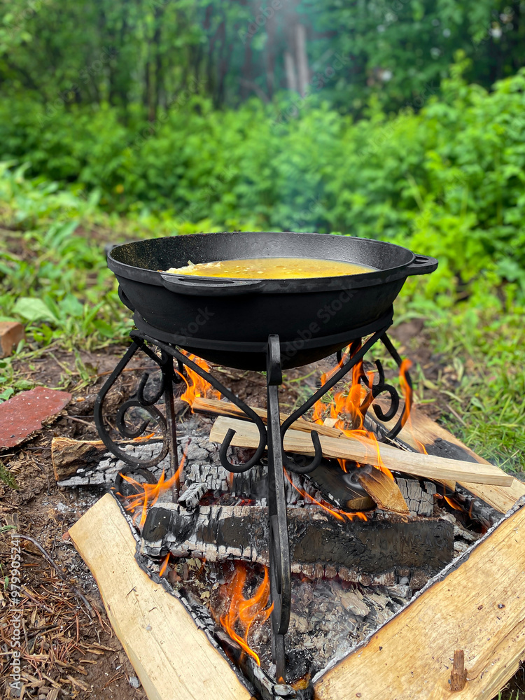 Cooking in cast-iron cauldron over a campfire. Pilaf or soup in cauldron. Vertical Cooking in cast-iron cauldron over a campfire. Pilaf or soup in cauldron. Vertical