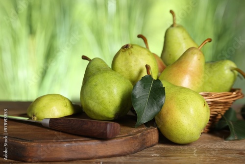 Fresh pears and leaves on wooden table against blurred green background