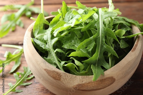Fresh green arugula leaves in bowl on wooden table, closeup