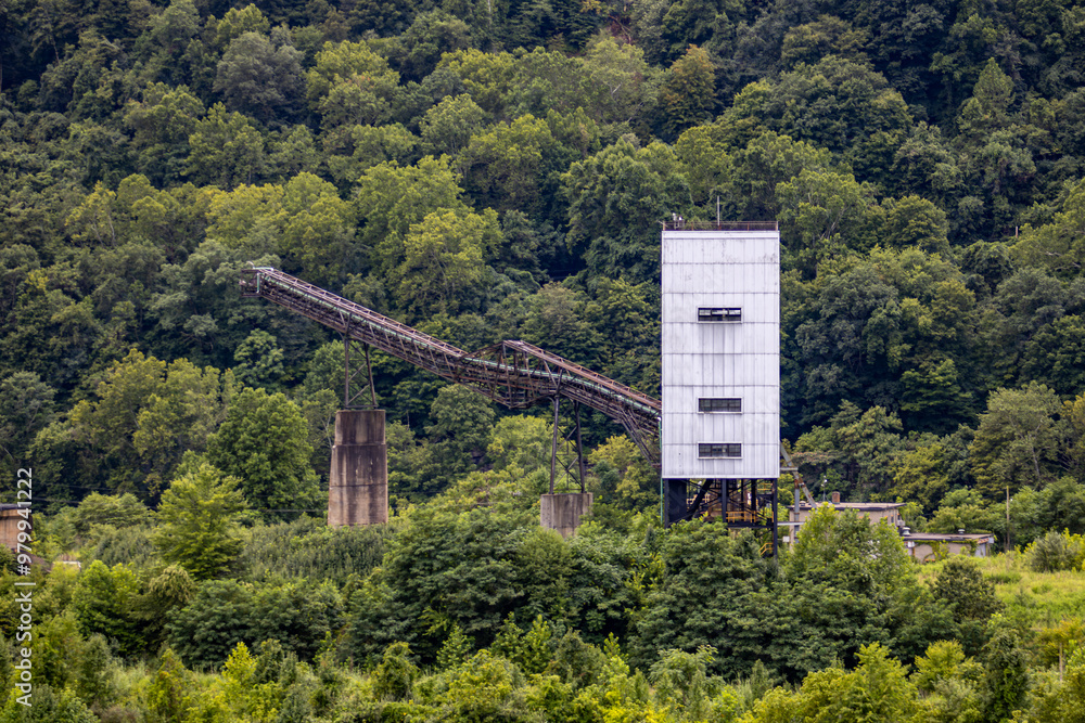 Obraz premium Abandoned Industrial Mining Structure with Conveyor Belt in Forested Area.
