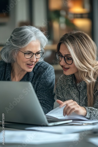 Collaborative teamwork between two business women in their thirties and older discussing project details using a laptop in an office setting