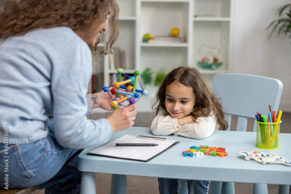 Cute girl sitting at the table while having a speech therapy tutorial and smiling nicely Cute girl sitting at the table while having a speech therapy tutorial and smiling nicely